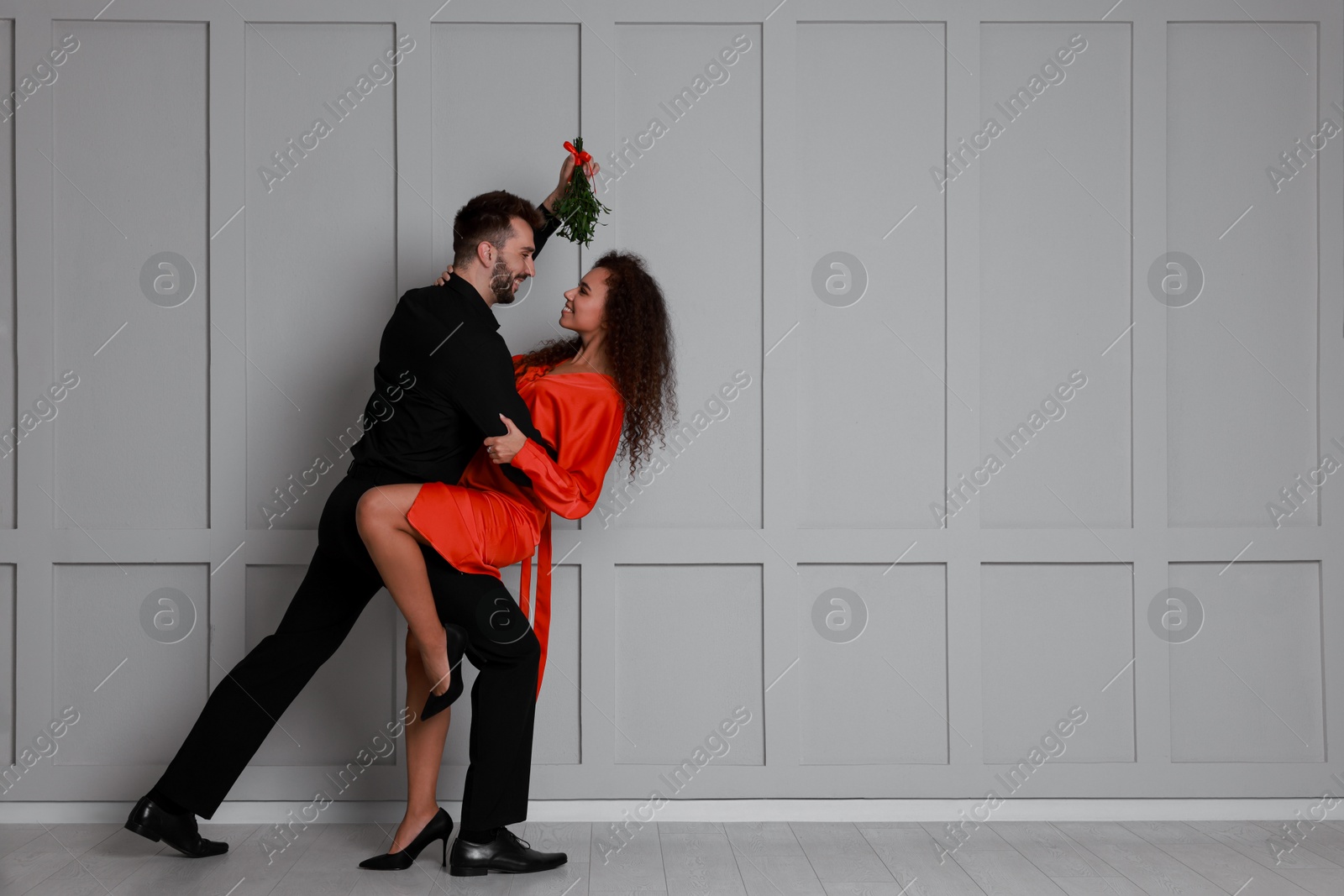 Photo of Lovely couple dancing under mistletoe bunch near light grey wall. Space for text