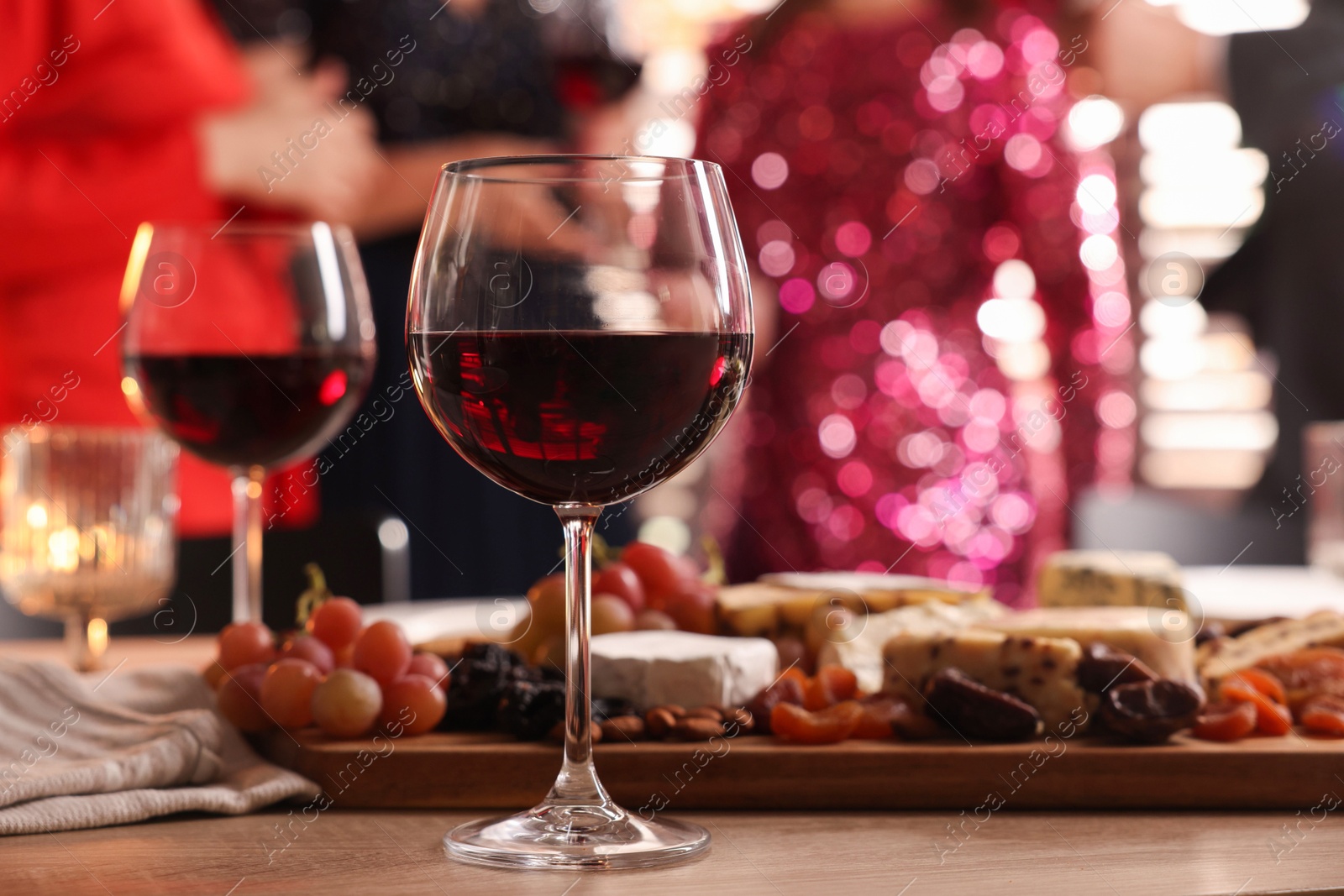 Photo of People holding glasses of wine at party, focus on wooden table with snacks and alcohol