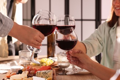 Photo of People clinking glasses of red wine at served table, closeup