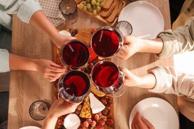 Photo of People clinking glasses of red wine at served table, top view