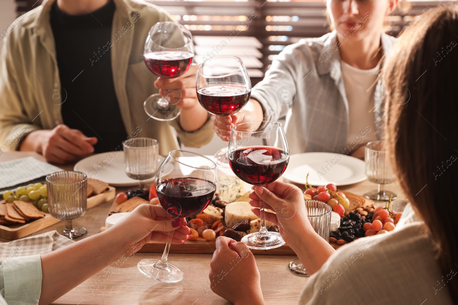 Photo of People clinking glasses of red wine at served table, closeup