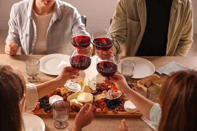 Photo of People clinking glasses of red wine at served table, closeup