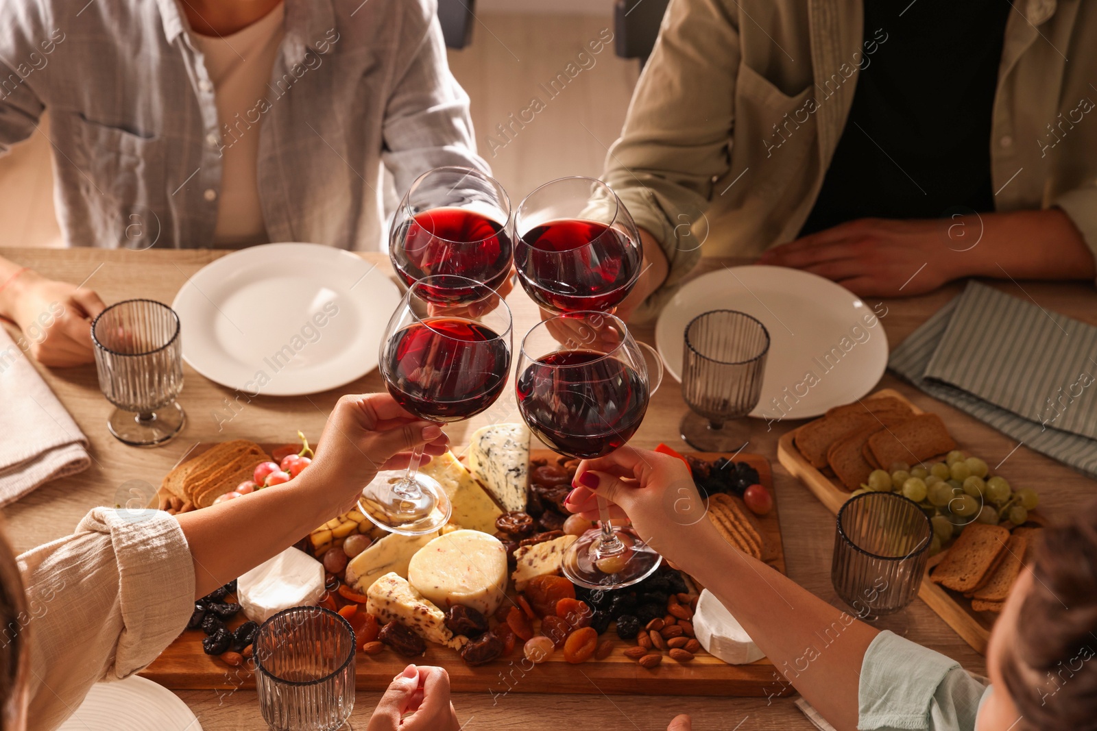 Photo of People clinking glasses of red wine at served table, closeup