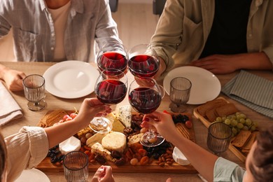 Photo of People clinking glasses of red wine at served table, closeup