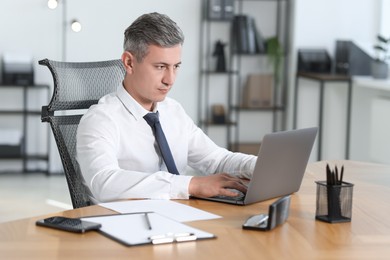 Photo of Businessman working on laptop at table in office