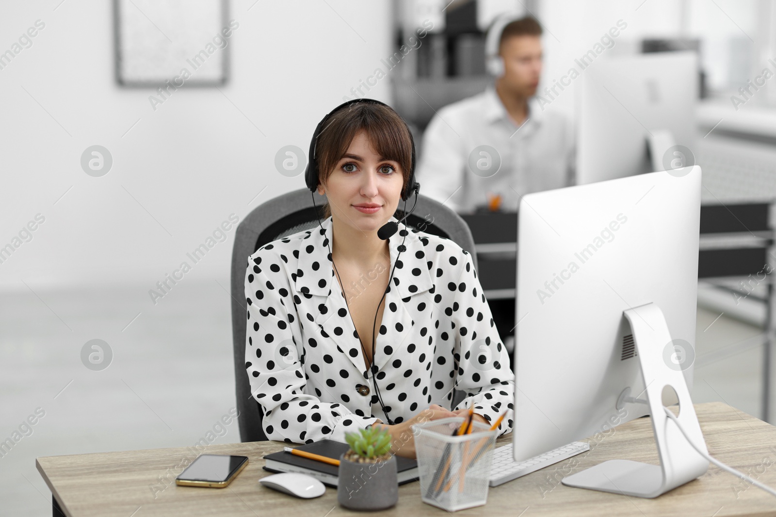 Photo of Saleswoman talking to client via headset at desk in office