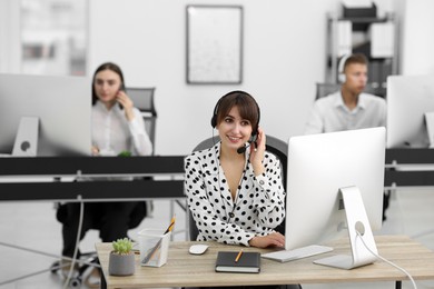 Photo of Saleswoman talking to client via headset at desk in office