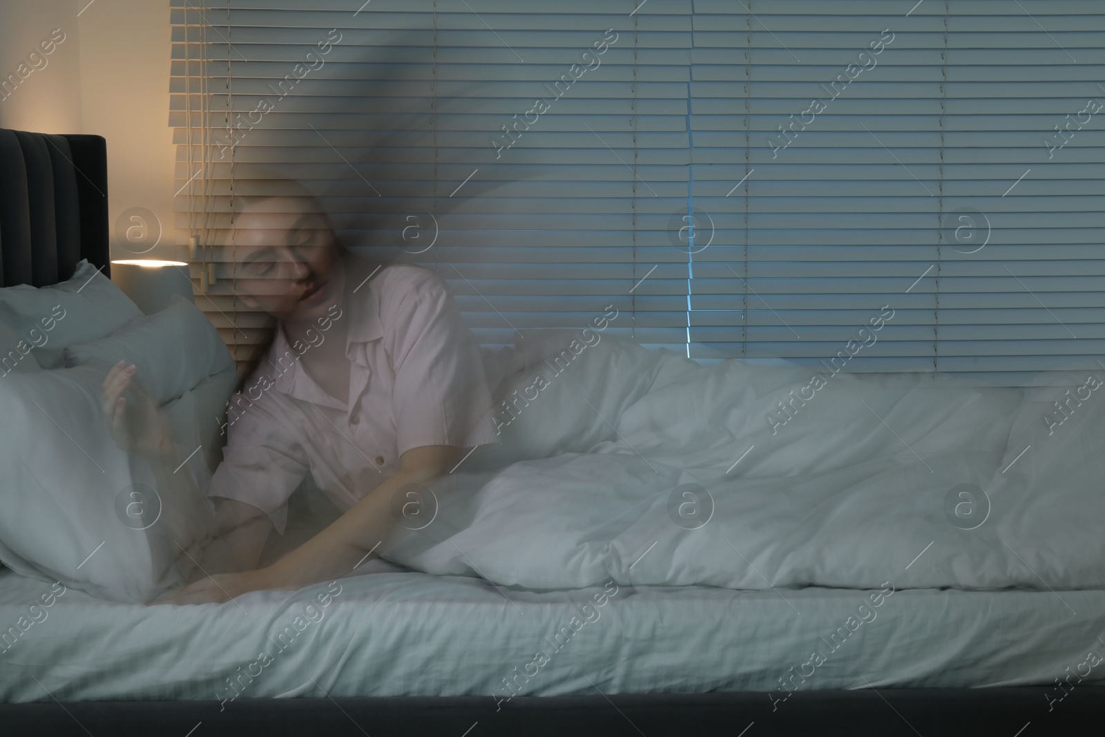 Photo of Young woman suffering from sleepwalking on bed at home, long-exposure