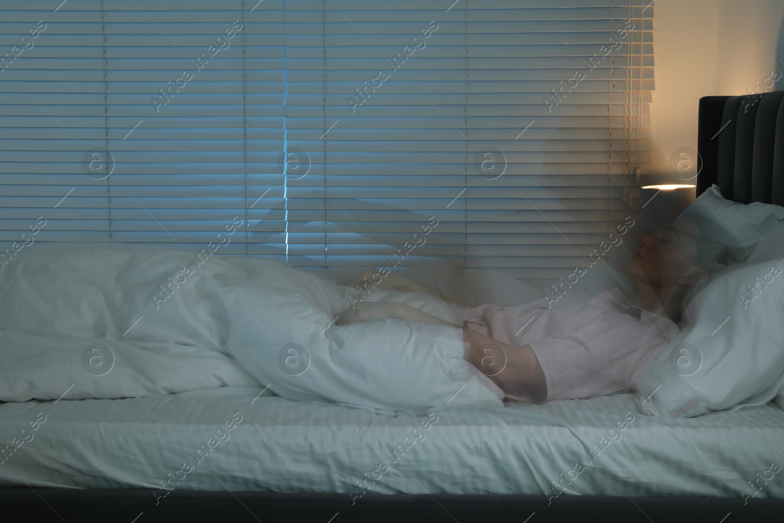 Photo of Young woman suffering from sleepwalking on bed at home, long-exposure