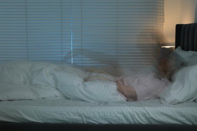 Young woman suffering from sleepwalking on bed at home, long-exposure