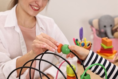 Photo of Autism therapy. Smiling psychologist and little girl playing with educational toy in mental health center, closeup