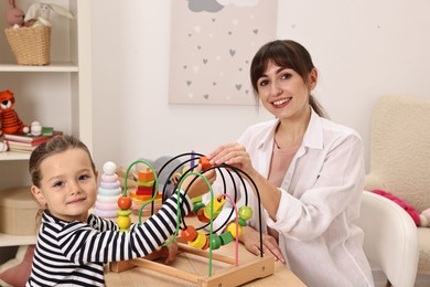 Photo of Autism therapy. Smiling psychologist and little girl playing with educational toy at table in mental health center