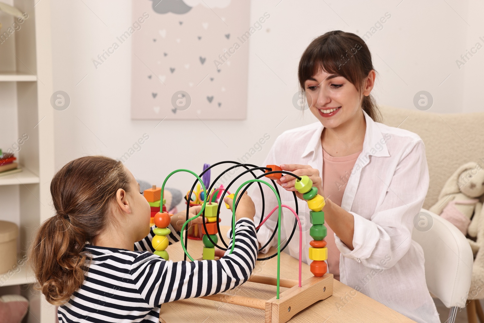 Photo of Autism therapy. Smiling psychologist and little girl playing with educational toy at table in mental health center