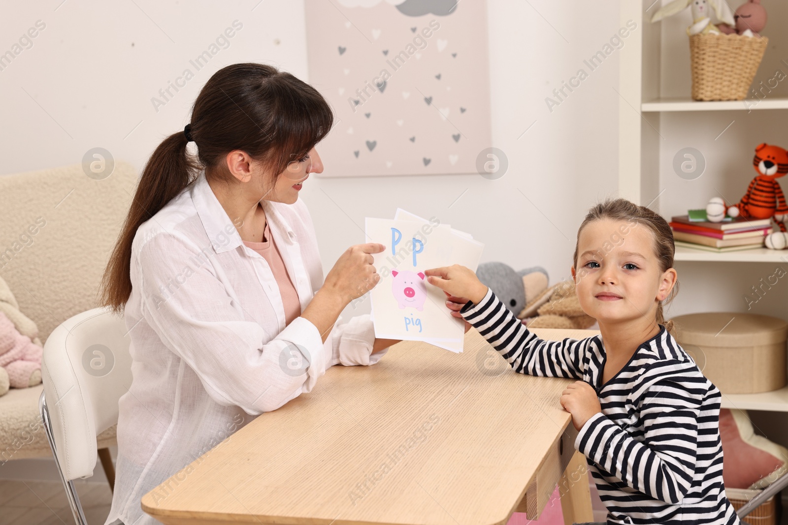 Photo of Speech therapist working with little girl at table in autism treatment center