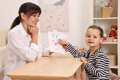 Photo of Smiling speech therapist working with little girl at table in autism treatment center