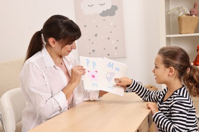 Speech therapist working with little girl at table in autism treatment center