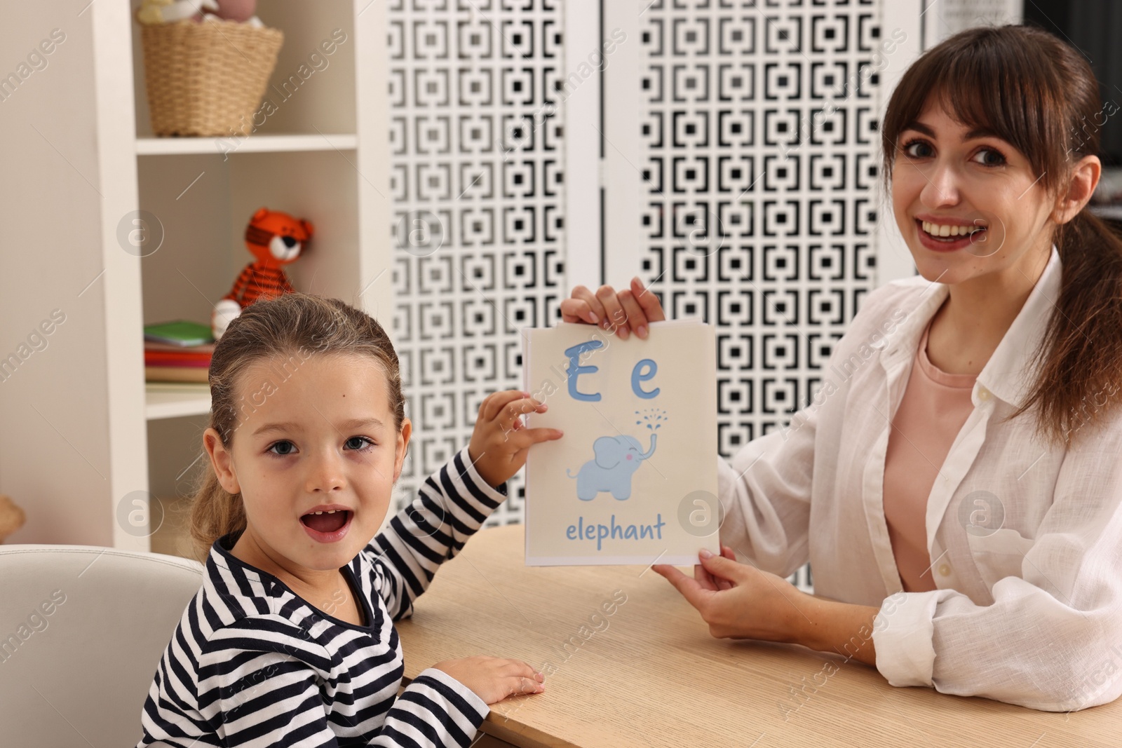 Photo of Smiling speech therapist working with little girl at table in autism treatment center