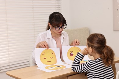 Photo of Autism therapy. Little girl choosing emoticon at table with psychologist in mental health center