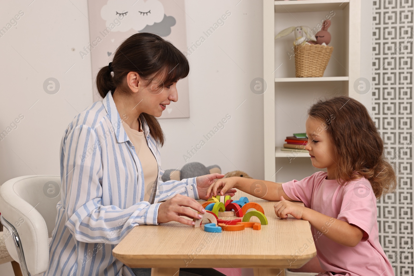 Photo of Autism therapy. Smiling psychologist and little girl playing with educational toy at table in mental health center