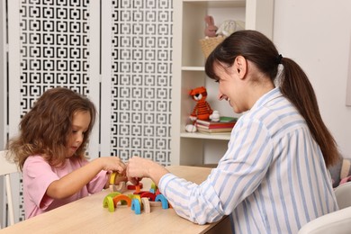 Autism therapy. Smiling psychologist and little girl playing with educational toy at table in mental health center