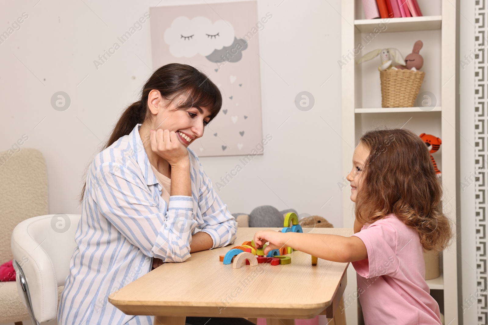 Photo of Autism therapy. Smiling psychologist and little girl playing with educational toy at table in mental health center