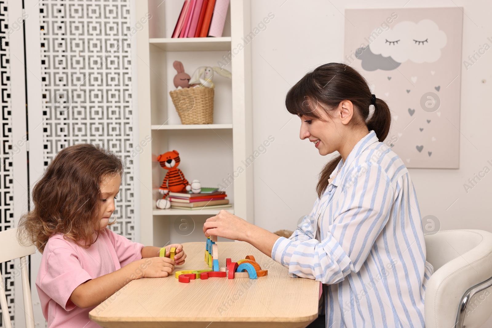 Photo of Autism therapy. Smiling psychologist and little girl playing with educational toy at table in mental health center