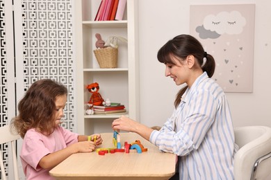 Photo of Autism therapy. Smiling psychologist and little girl playing with educational toy at table in mental health center