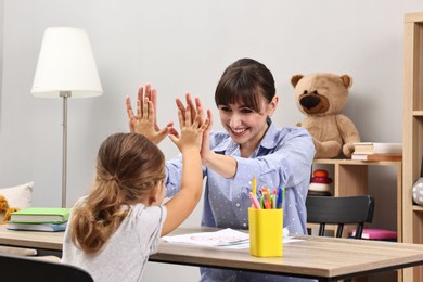 Photo of Autism therapy. Smiling psychologist giving high five to little girl at table in mental health center