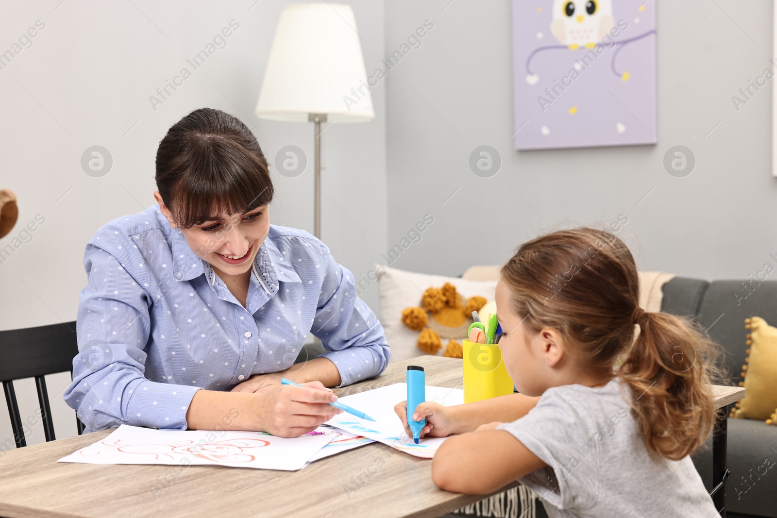 Photo of Autism therapy. Smiling psychologist and little girl drawing pictures at table in mental health center