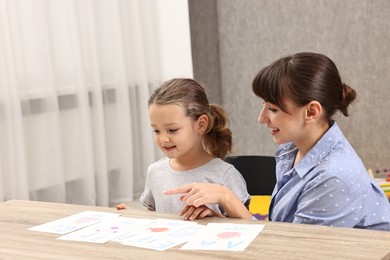 Photo of Smiling speech therapist working with little girl at table in autism treatment center. Space for text