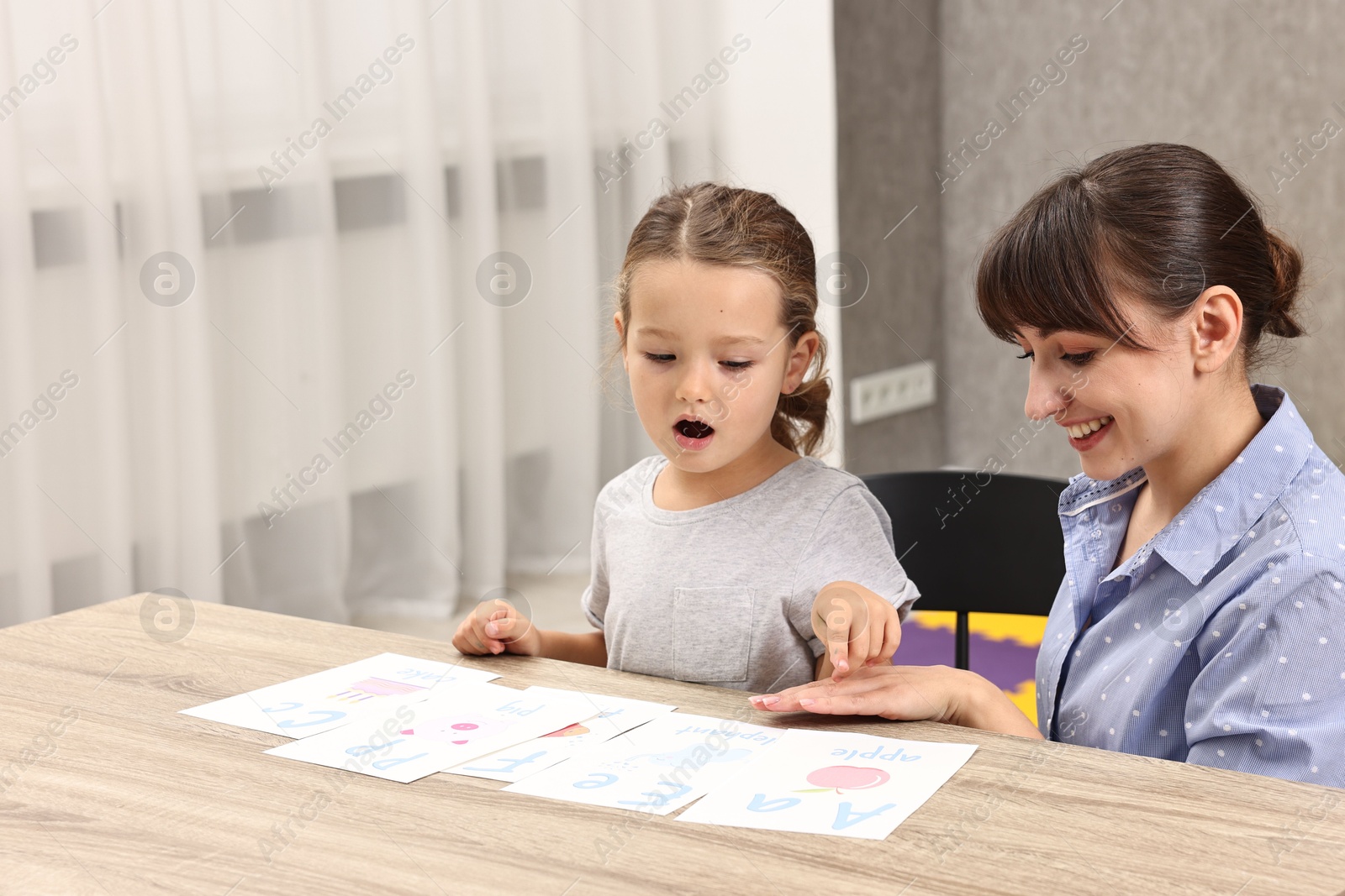 Photo of Smiling speech therapist working with little girl at table in autism treatment center. Space for text