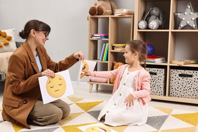 Photo of Autism therapy. Little girl choosing emoticon with smiling psychologist in mental health center