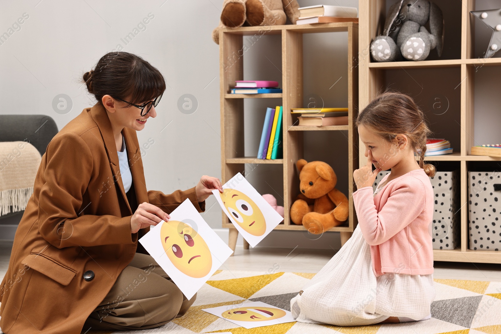 Photo of Autism therapy. Little girl choosing emoticon with smiling psychologist in mental health center