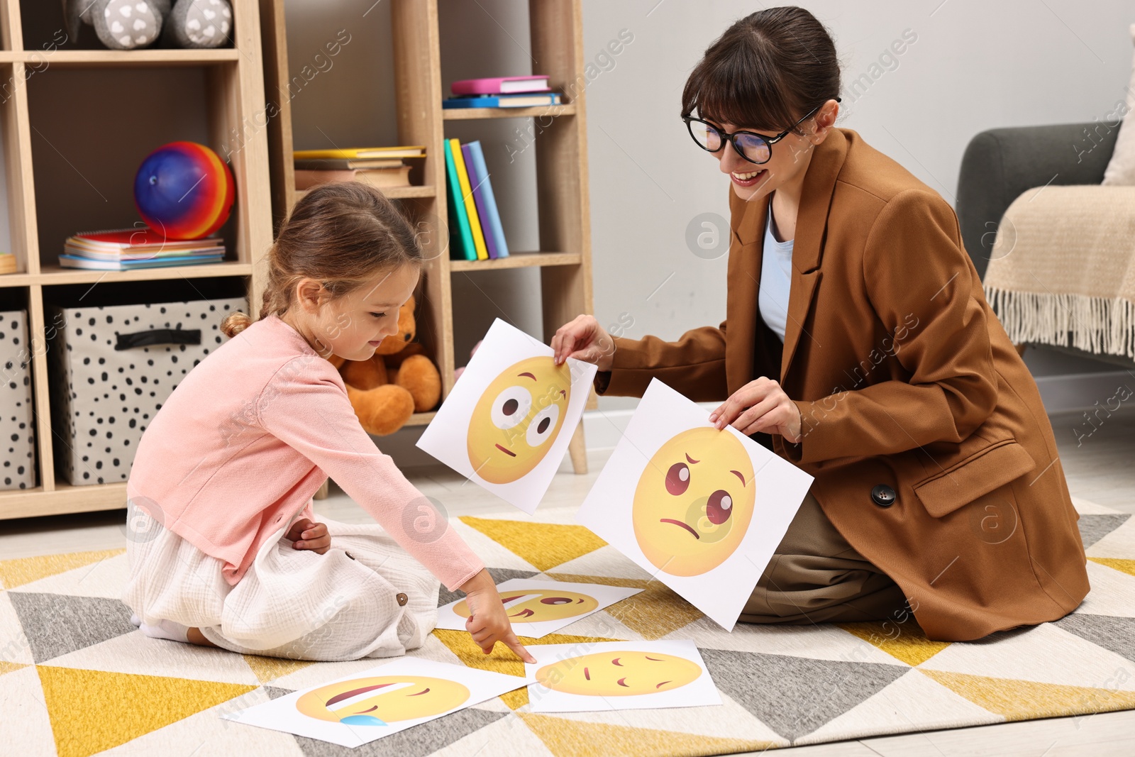 Photo of Autism therapy. Little girl choosing emoticon with smiling psychologist in mental health center