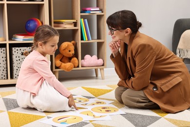 Photo of Autism therapy. Little girl choosing emoticon with smiling psychologist in mental health center