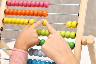 Photo of Autism therapy. Psychologist and little girl playing with wooden abacus indoors, closeup