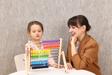 Photo of Autism therapy. Smiling psychologist and little girl playing with wooden abacus indoors