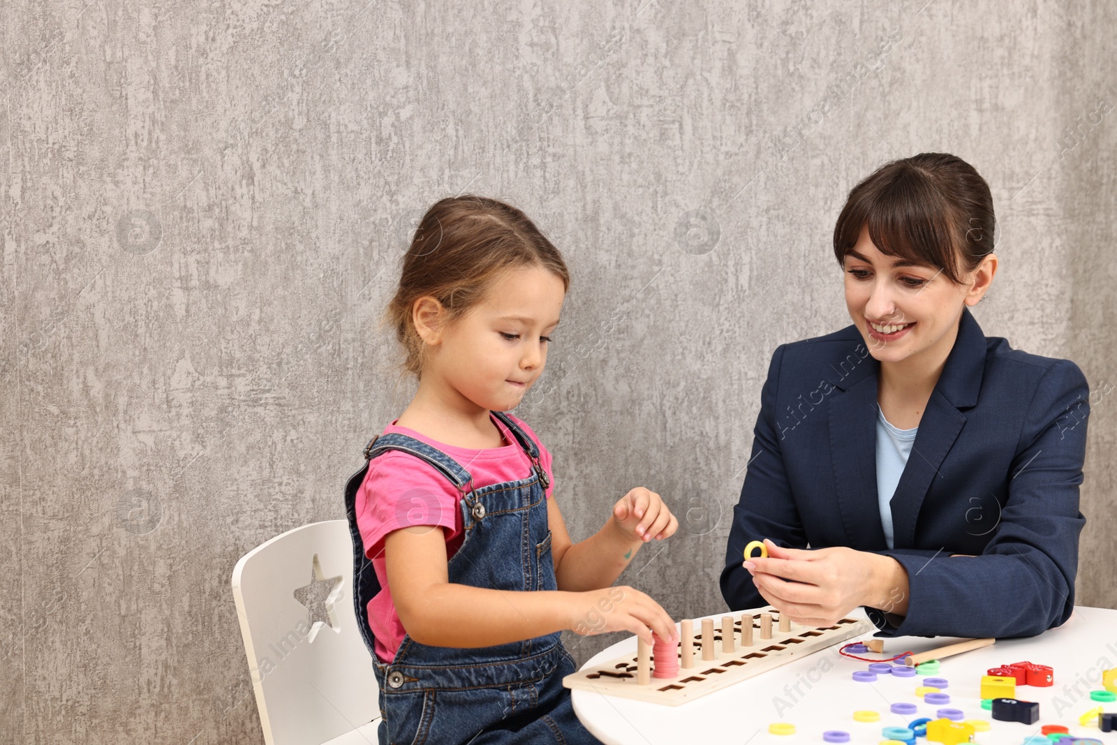 Photo of Autism therapy. Smiling psychologist and little girl playing with educational toy at table in mental health center