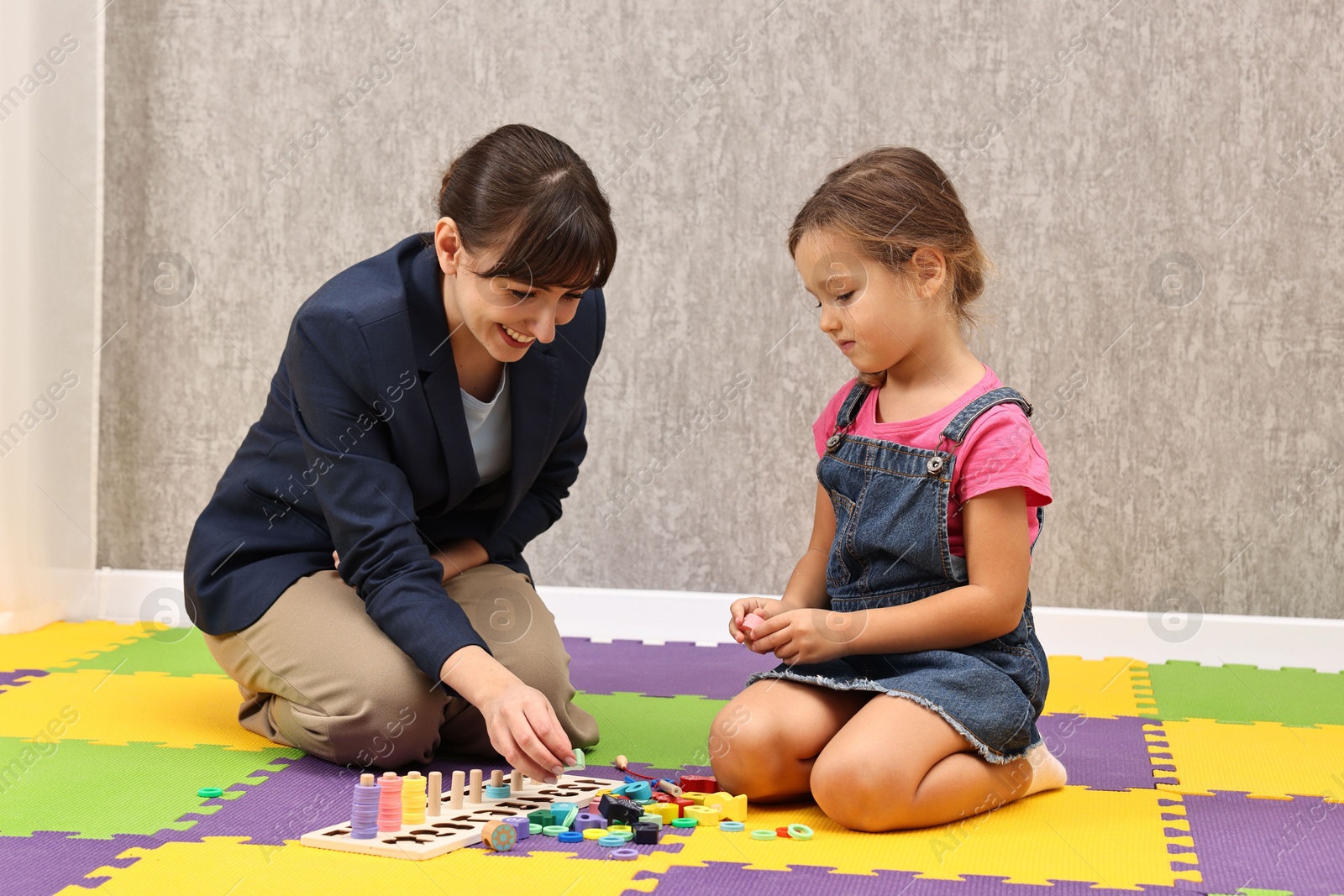 Photo of Autism therapy. Smiling psychologist and little girl playing with educational toy in mental health center