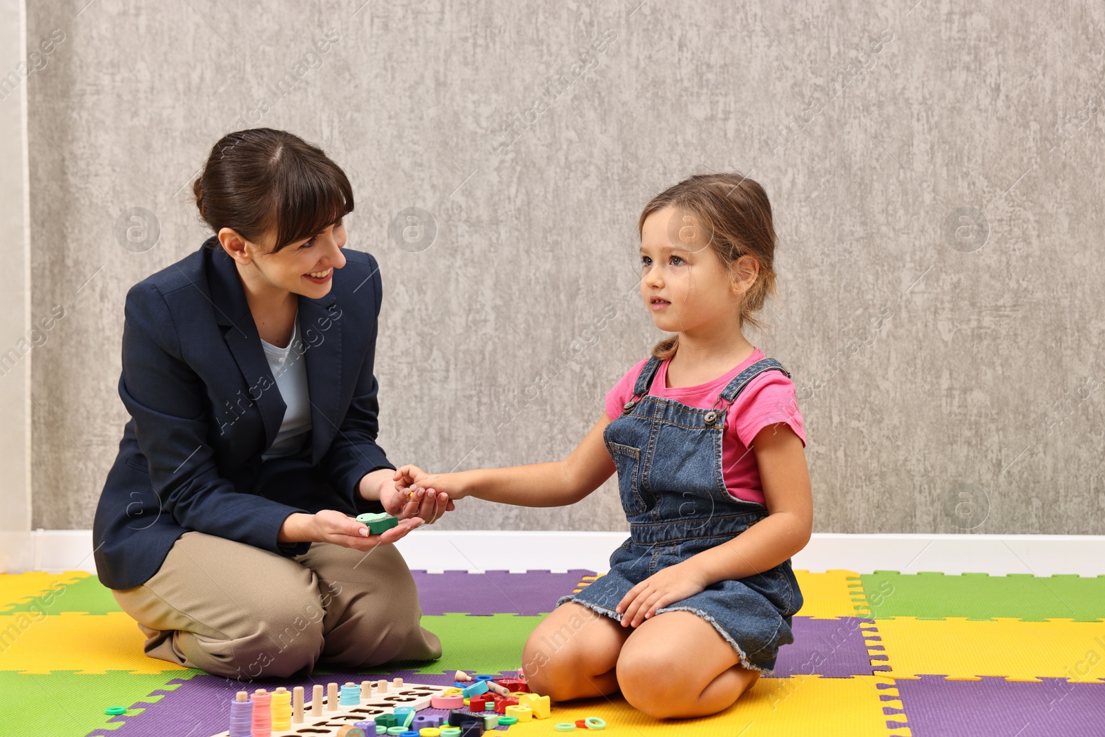 Photo of Autism therapy. Smiling psychologist and little girl playing with educational toy in mental health center