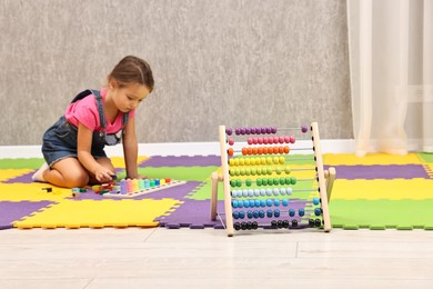 Photo of Autism therapy. Little girl playing with educational toy on floor in mental health center, focus on abacus