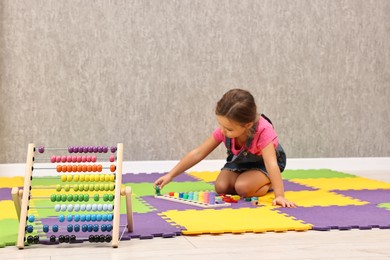 Photo of Autism therapy. Little girl playing with educational toy on floor in mental health center, focus on abacus