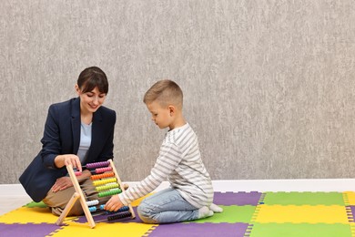 Photo of Autism therapy. Smiling psychologist and little boy playing with abacus in mental health center, space for text