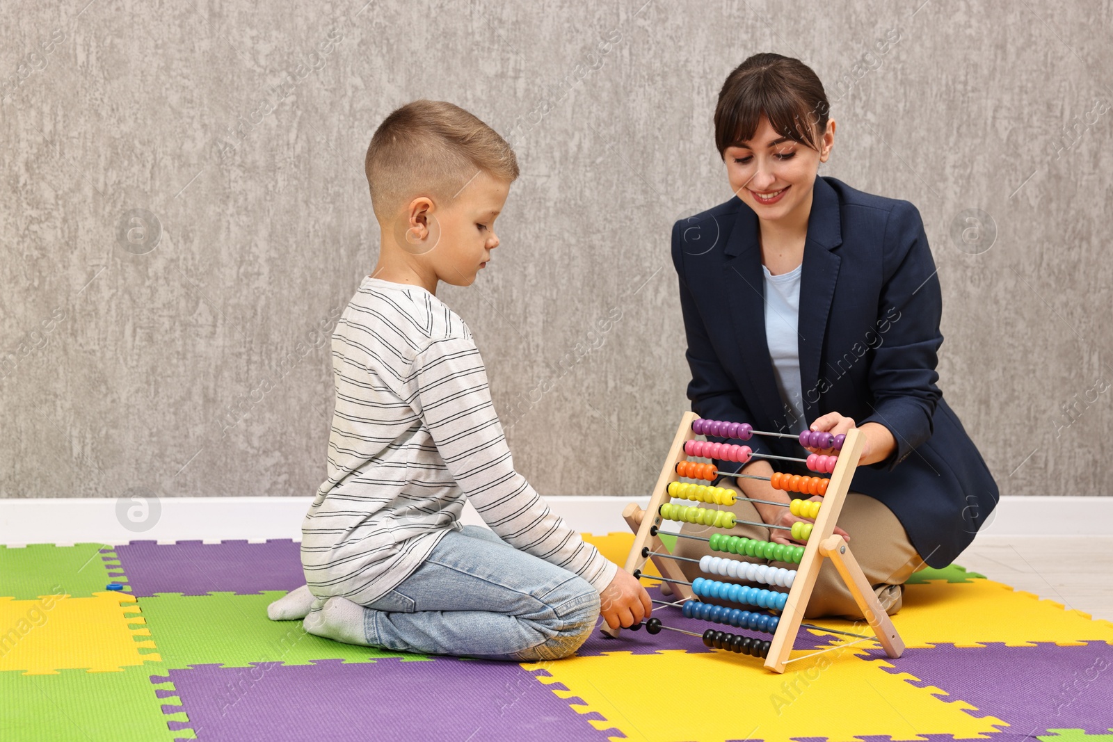 Photo of Autism therapy. Smiling psychologist and little boy playing with abacus in mental health center