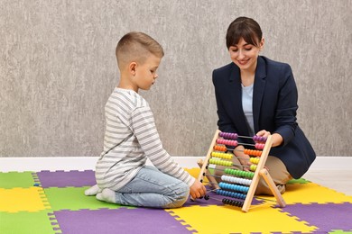 Photo of Autism therapy. Smiling psychologist and little boy playing with abacus in mental health center