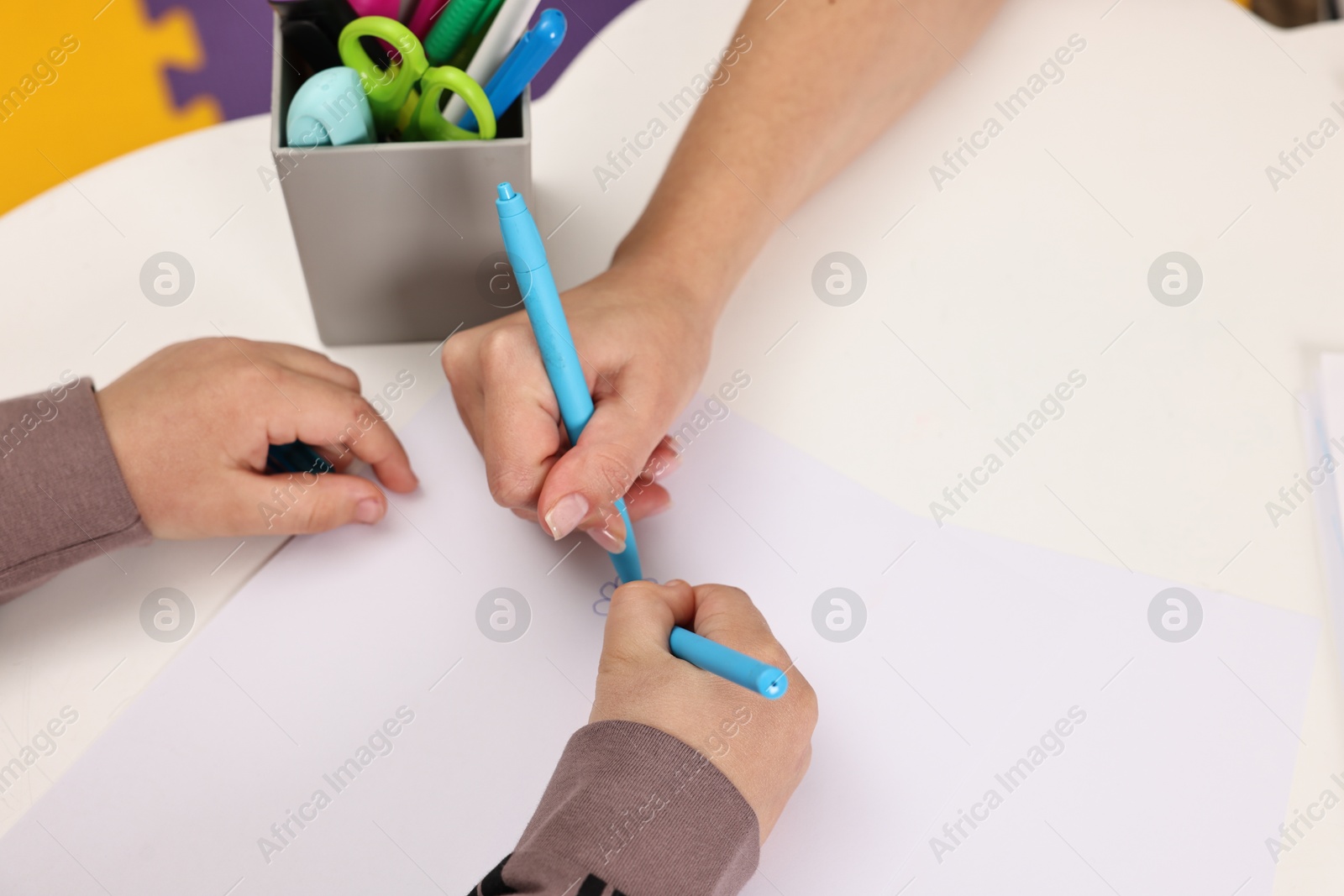 Photo of Autism therapy. Psychologist and little boy drawing picture at table, closeup