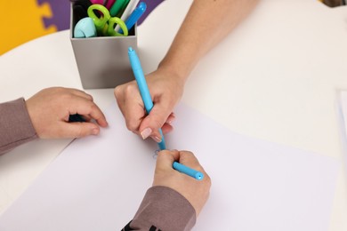 Photo of Autism therapy. Psychologist and little boy drawing picture at table, closeup