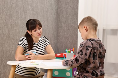 Autism therapy. Psychologist observing little boy drawing pictures at table in mental health center