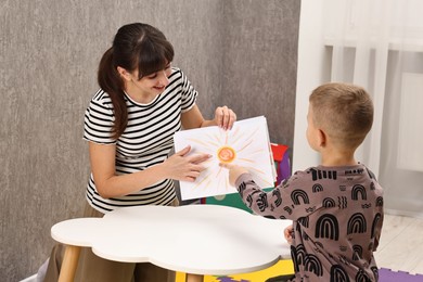 Photo of Autism therapy. Smiling psychologist working with little boy at table in mental health center