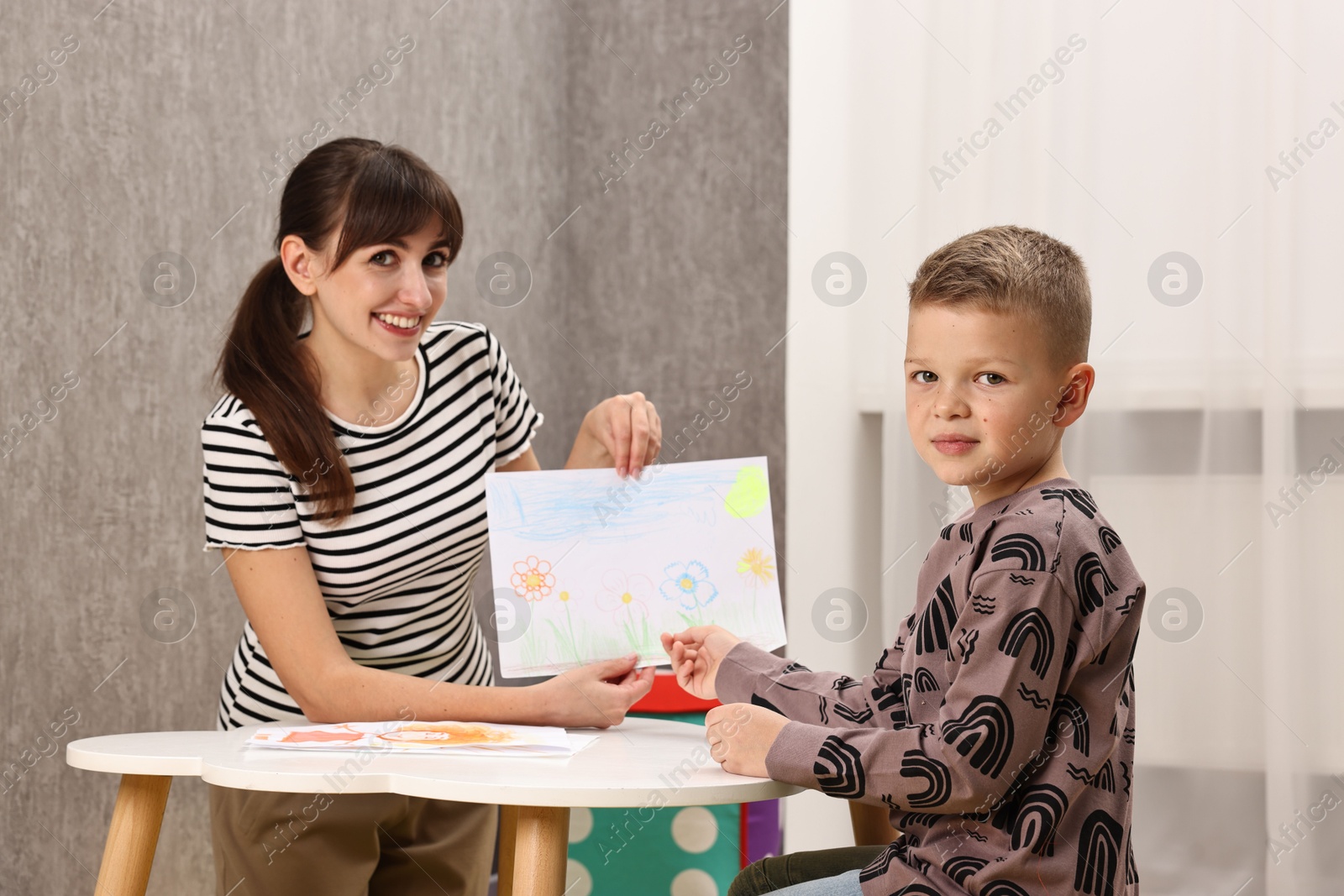 Photo of Autism therapy. Smiling psychologist working with little boy at table in mental health center